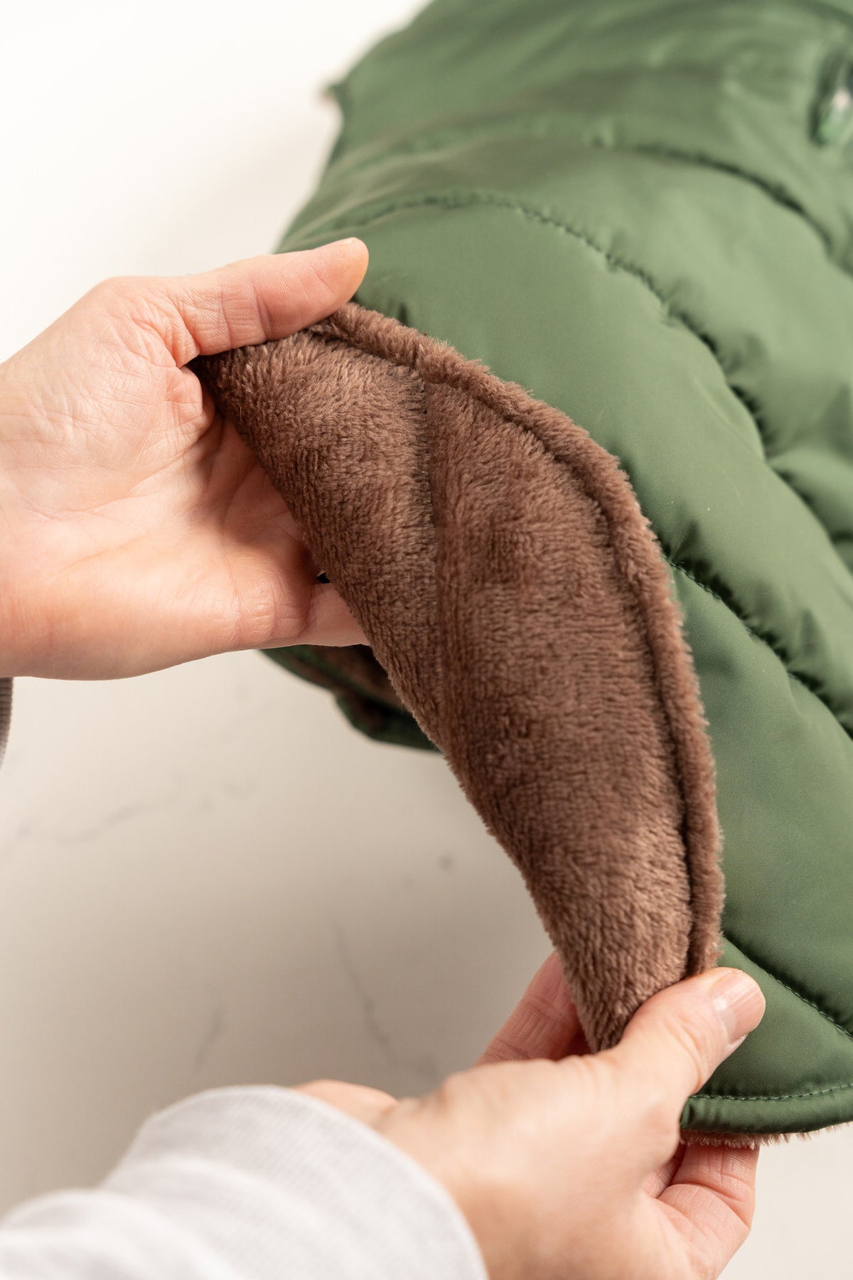Hands showing the thick plush taupe fleece lining of the Woodland Green dog puffer coat